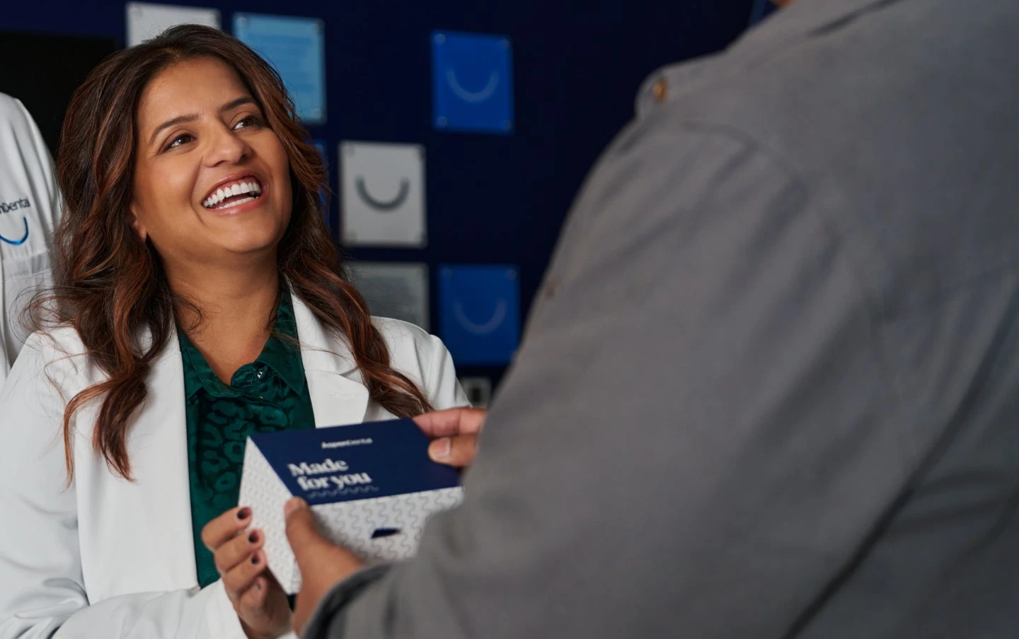 A cheerful Aspen Dental professional in a white coat hands a customized dental care package to a patient, highlighting a warm and welcoming interaction in a modern clinic environment.